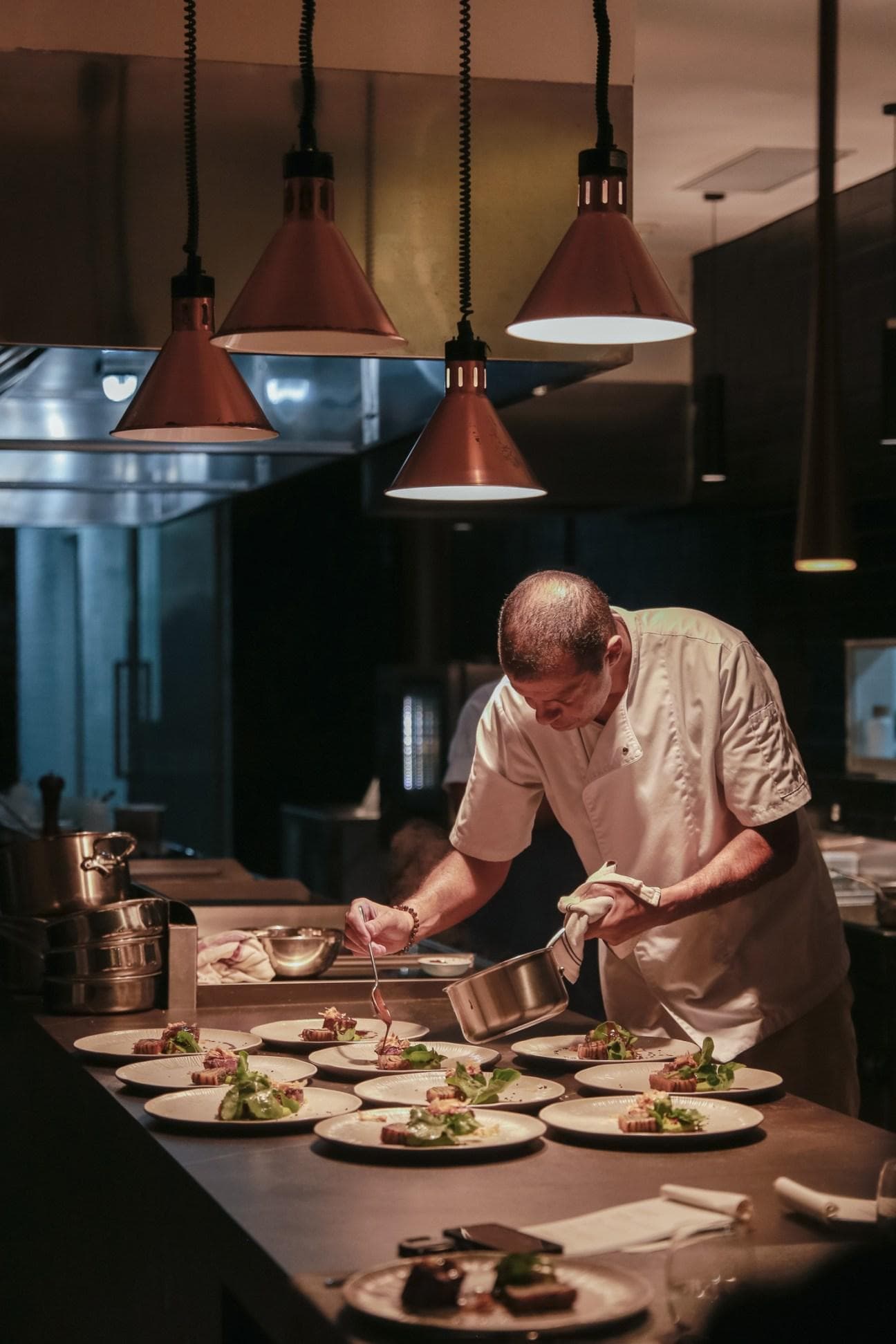 A cook finishing a plate at the pass under warm light