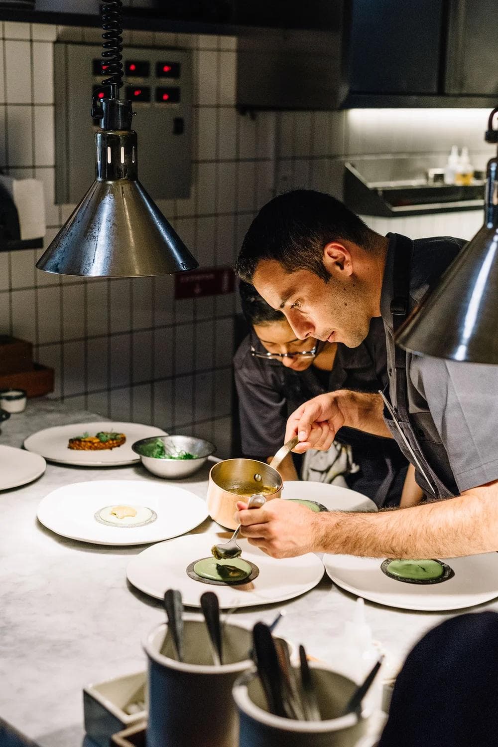 Two chefs finishing a row of plates under the heat lamps