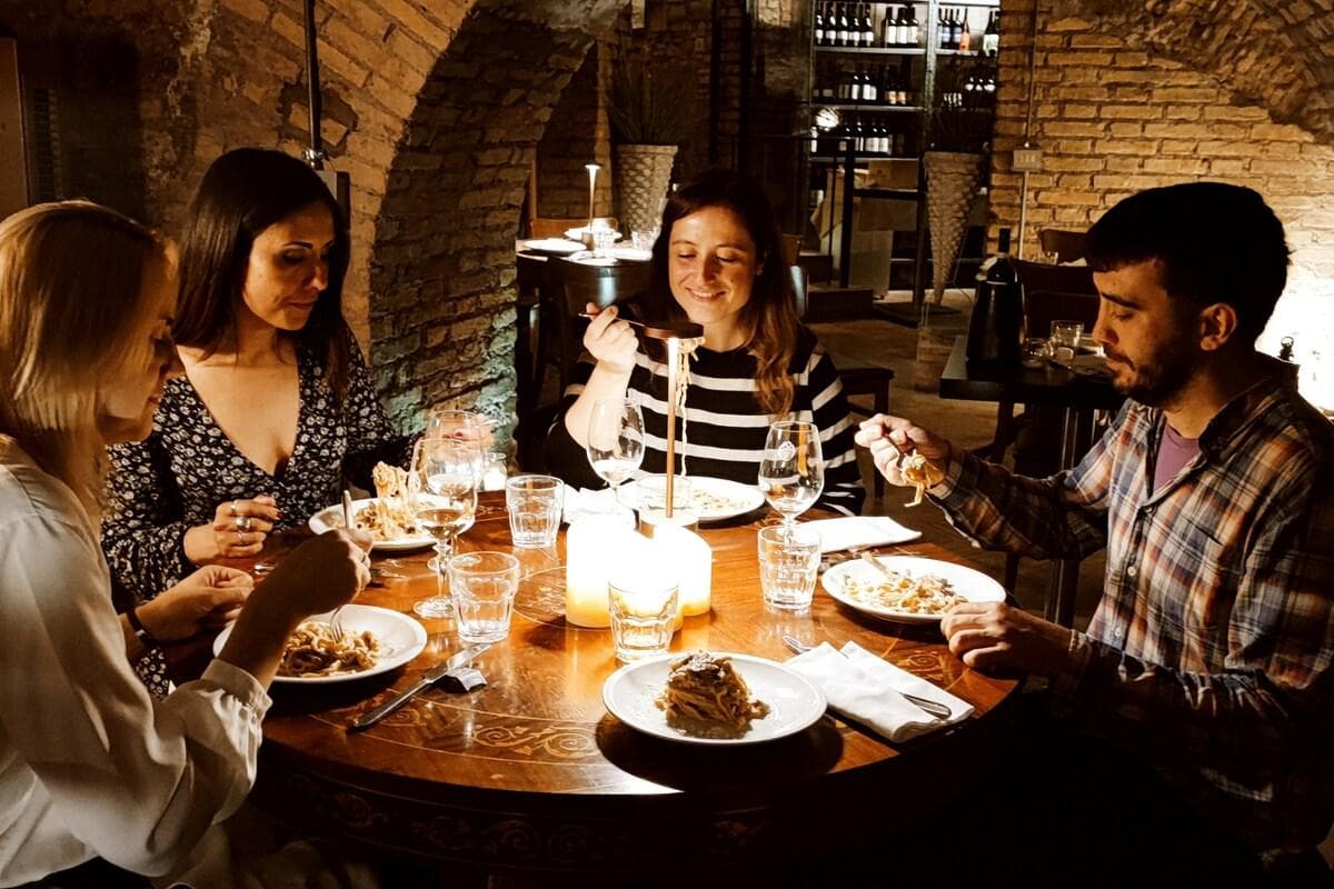 Five friends eating pasta around a table in the vaulted room