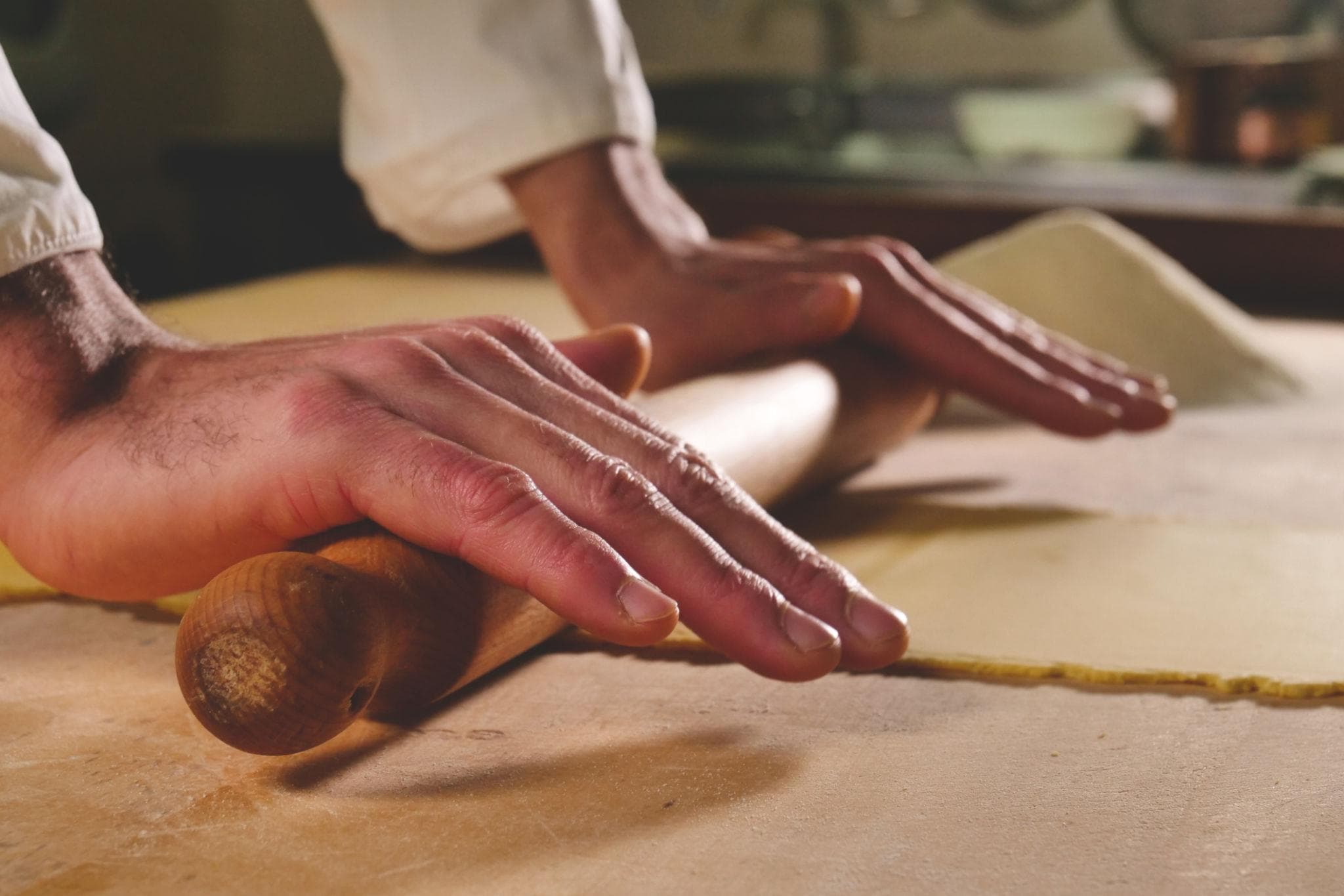Hands rolling a sheet of pasta dough flat with a wooden pin