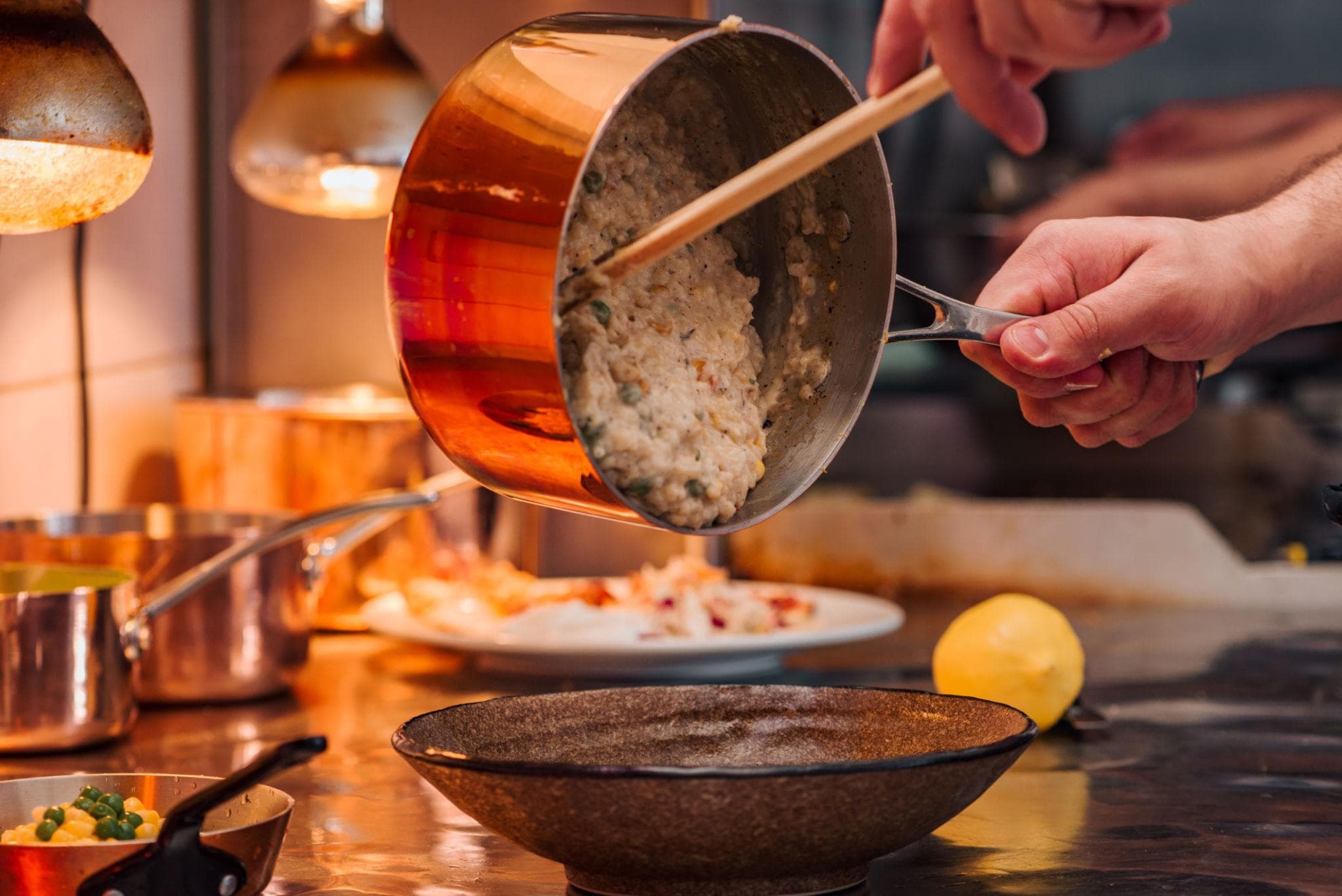 Risotto poured from a copper pan into a bowl at the stove